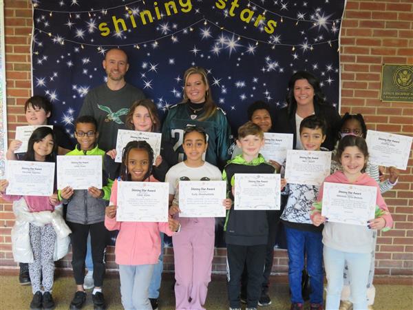 Children proudly display certificates in front of a wall.