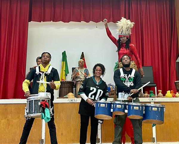 A multicultural ensemble standing around drums, enjoying a musical moment.