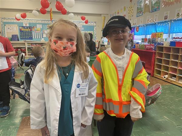 Two children in safety gear standing in classroom.