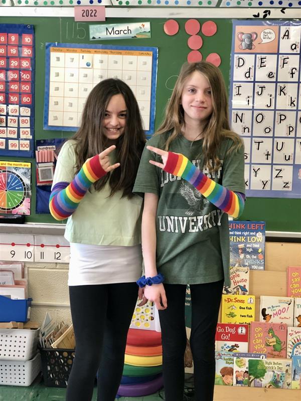 Two girls with rainbow arm bands smiling in classroom.