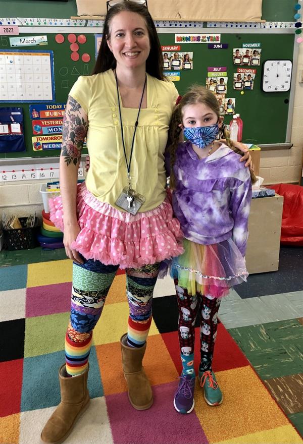 A woman and a girl in vibrant outfits standing side by side.