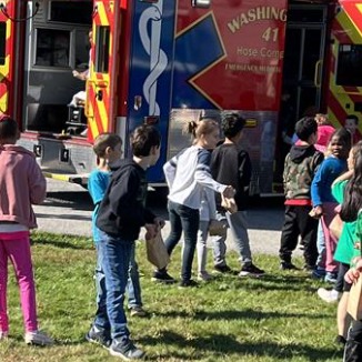 Kids playing near a fire truck on green grass.