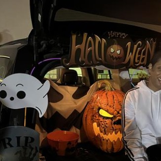 Woman sitting in car trunk with Halloween decor.