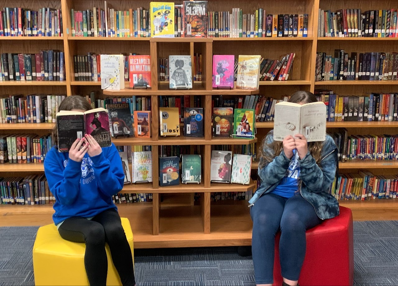 two kids sitting on yellow and red stools reading books