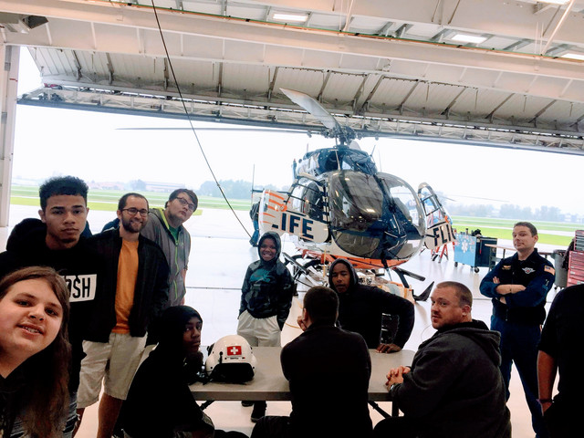 A group of people standing in front of a helicopter inside a hangar, posing for a photo.