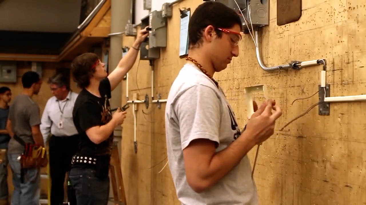 A team of individuals collaboratively installing electrical wiring in a well-lit room, focused on their tasks.