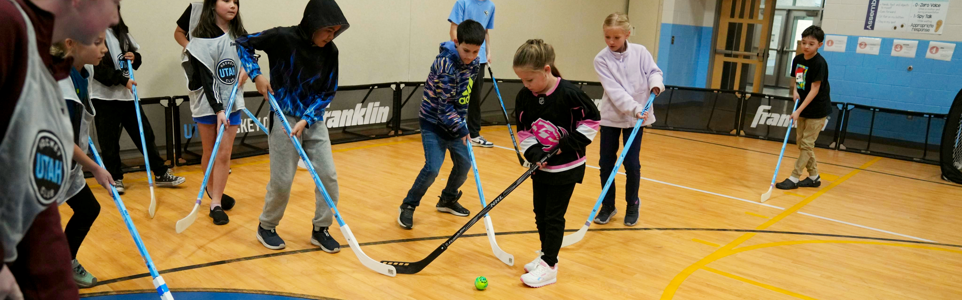 Elementary students playing street hockey in the gym.
