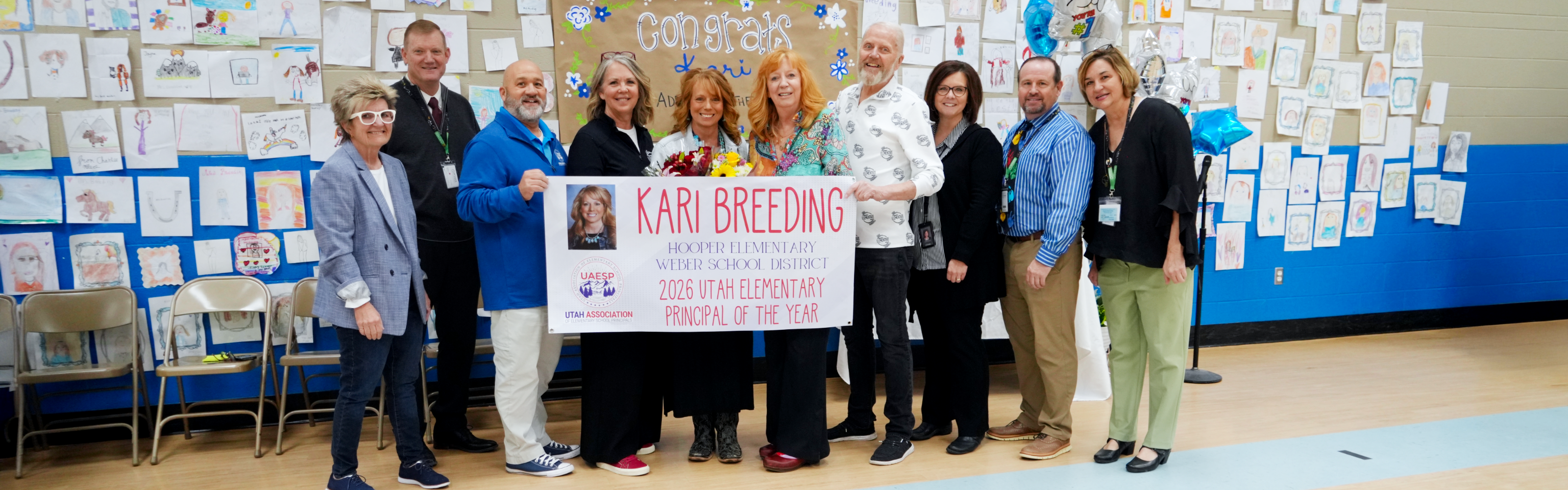 Weber School District leadership and staff standing together in the Hooper Elementary gym, holding a large banner that reads "Kari Breeding: 2026 Utah Elementary Principal of the Year."