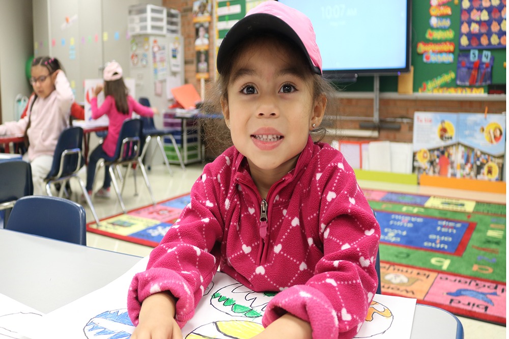 Young girl seated at a table in a classroom.