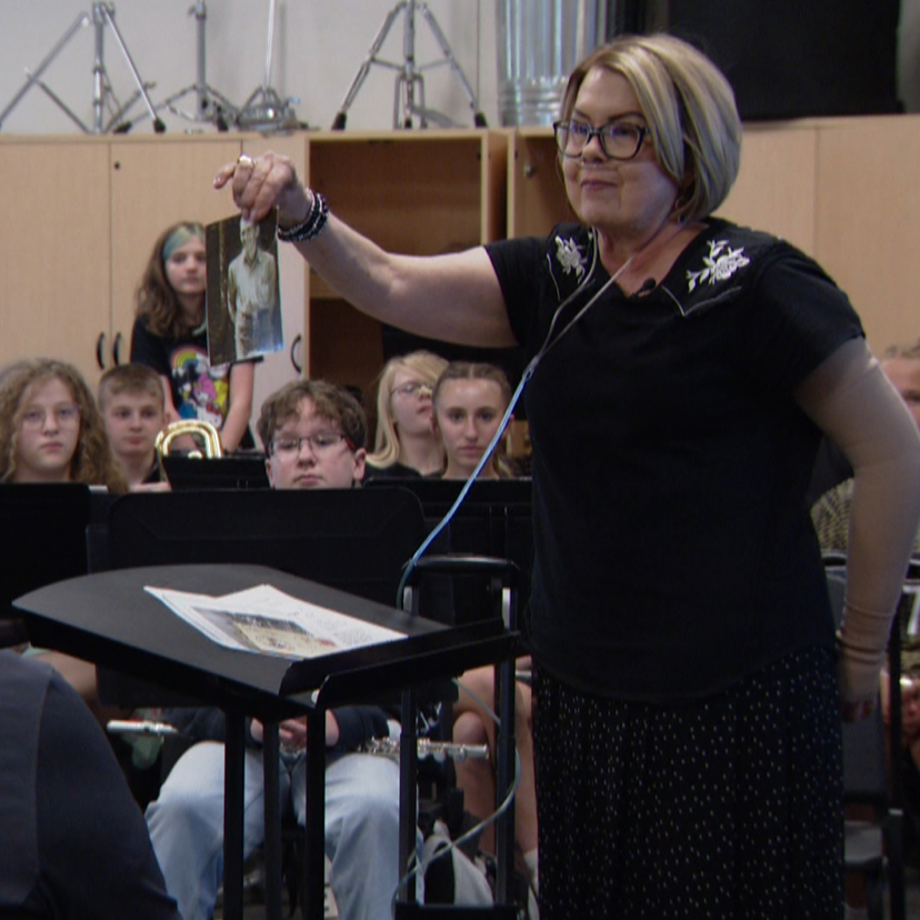 Janice Shannon (standing) holds a picture of her late father as she spoke to students about his old French horn that found a new home.