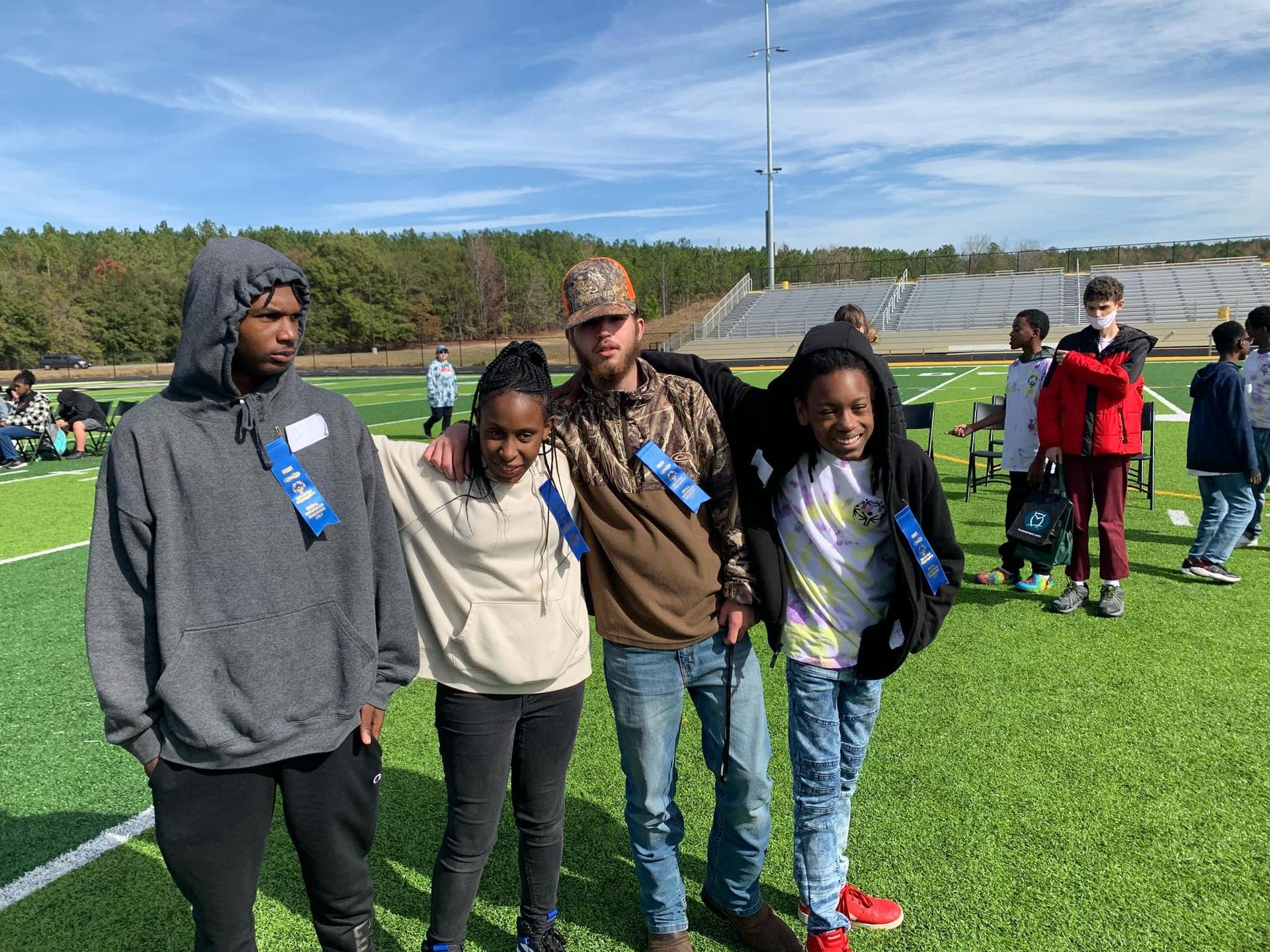 Four people posing for a photo at an outdoor event, standing on a grass field.