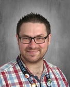 Photo Studio Picture of a Man with black hair wearing glasses an a pattern shirt with grey brackground 