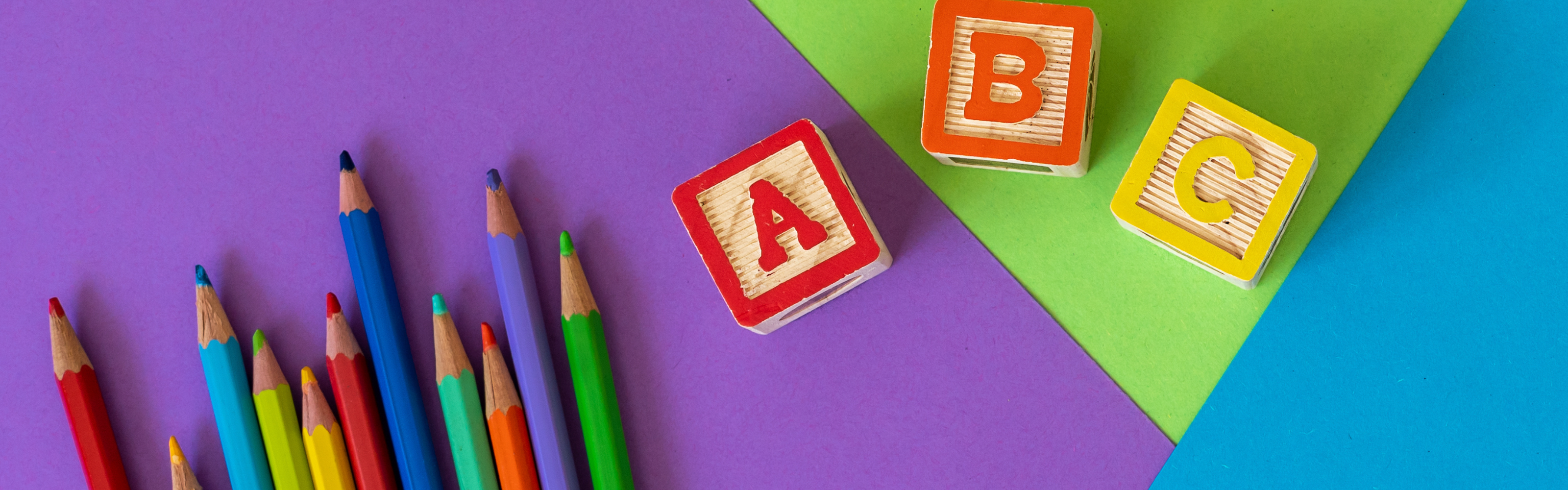 Colored pencils and alphabet blocks on a colorful background.