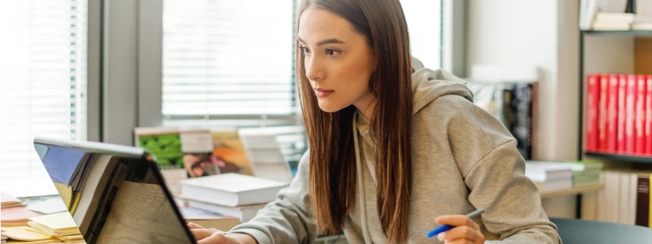 Woman sitting at a desk in a library with her laptop and books.