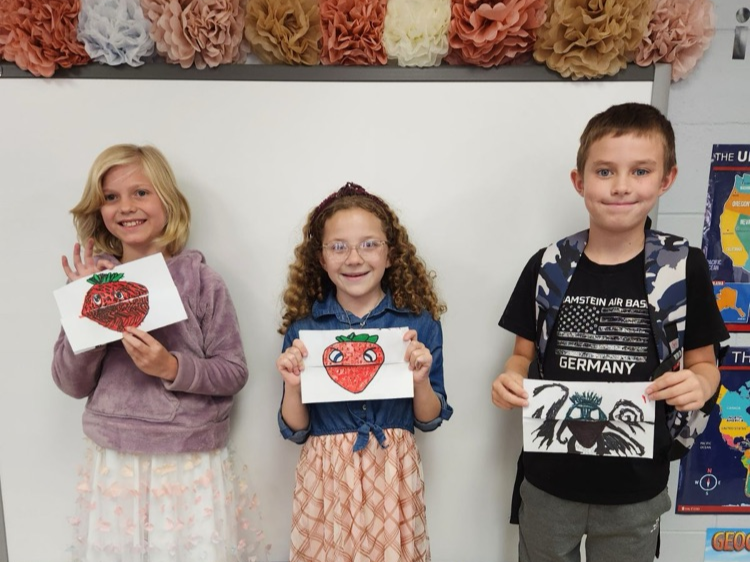 Three elementary students holding up and showing off their artwork made in art class