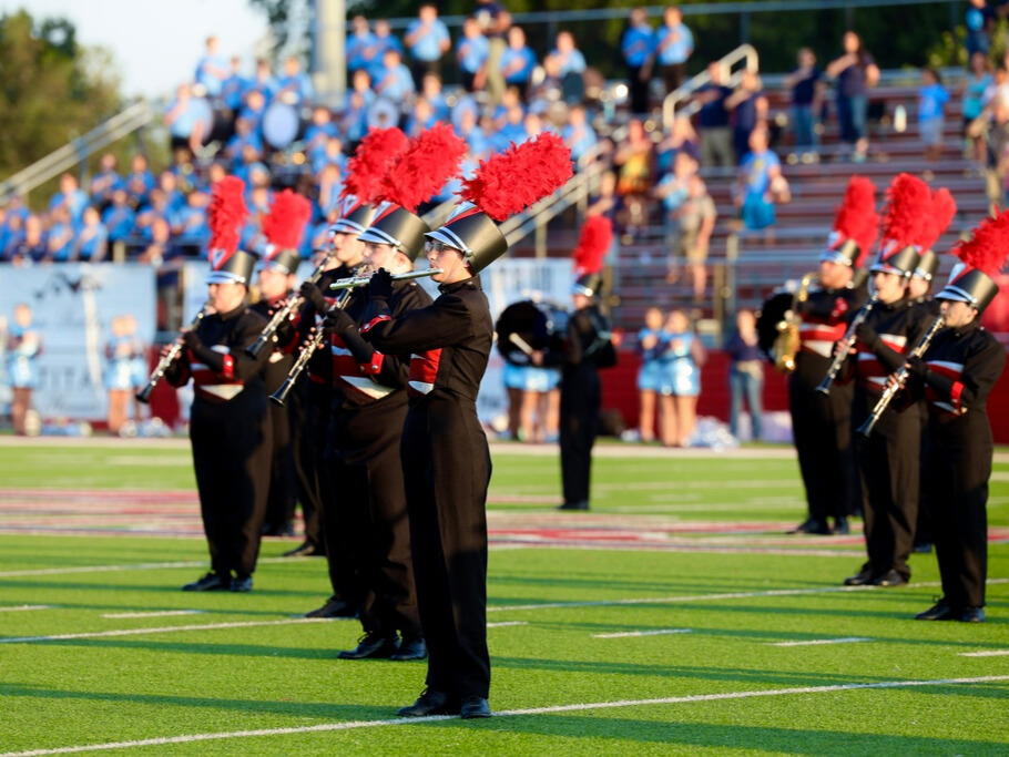 A close up of high school marching band students performing on a football field in black and red uniforms