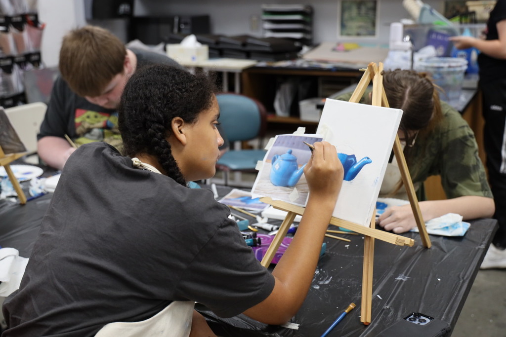 Art student painting a picture of a blue teapot 