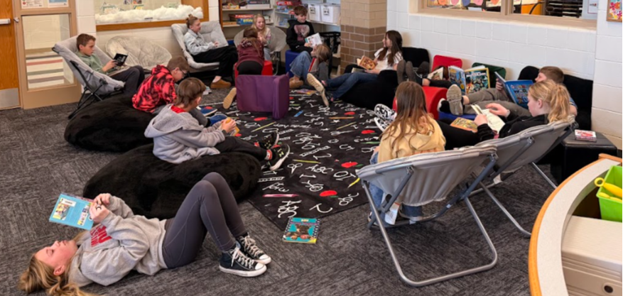 students in 5th grade are in library reading their books on the carpet and comfy chairs