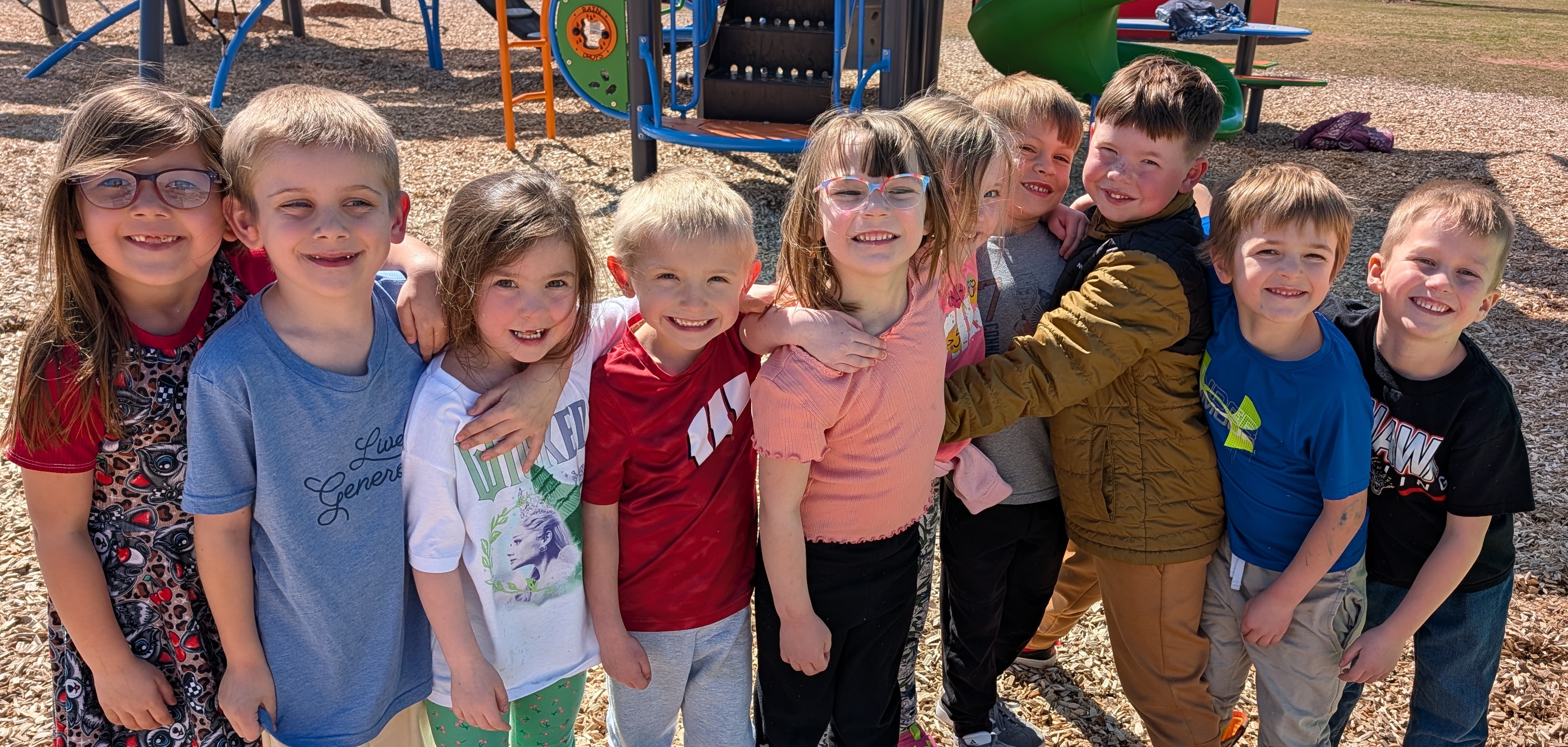 Kindergarten students outside posing for a group picture playground in the background 
