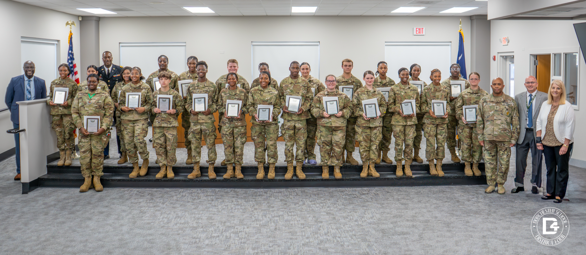 Woodland High School JROTC cadets stand with their wooden plaques on the board room steps alongside Principal Michael White, JROTC instructors, Superintendent Jeffrey Beckwith, and Board Chair Phyllis Hughes.