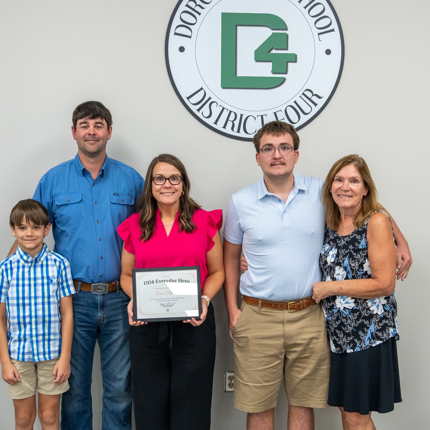 Nurse Peters and her family posing with her award standing under a DD4 logo in the Board Room.