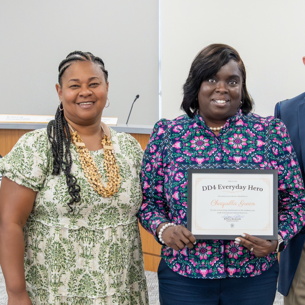 Mrs. Green posing with Dr. Jackson in the boardroom while holding her award. 