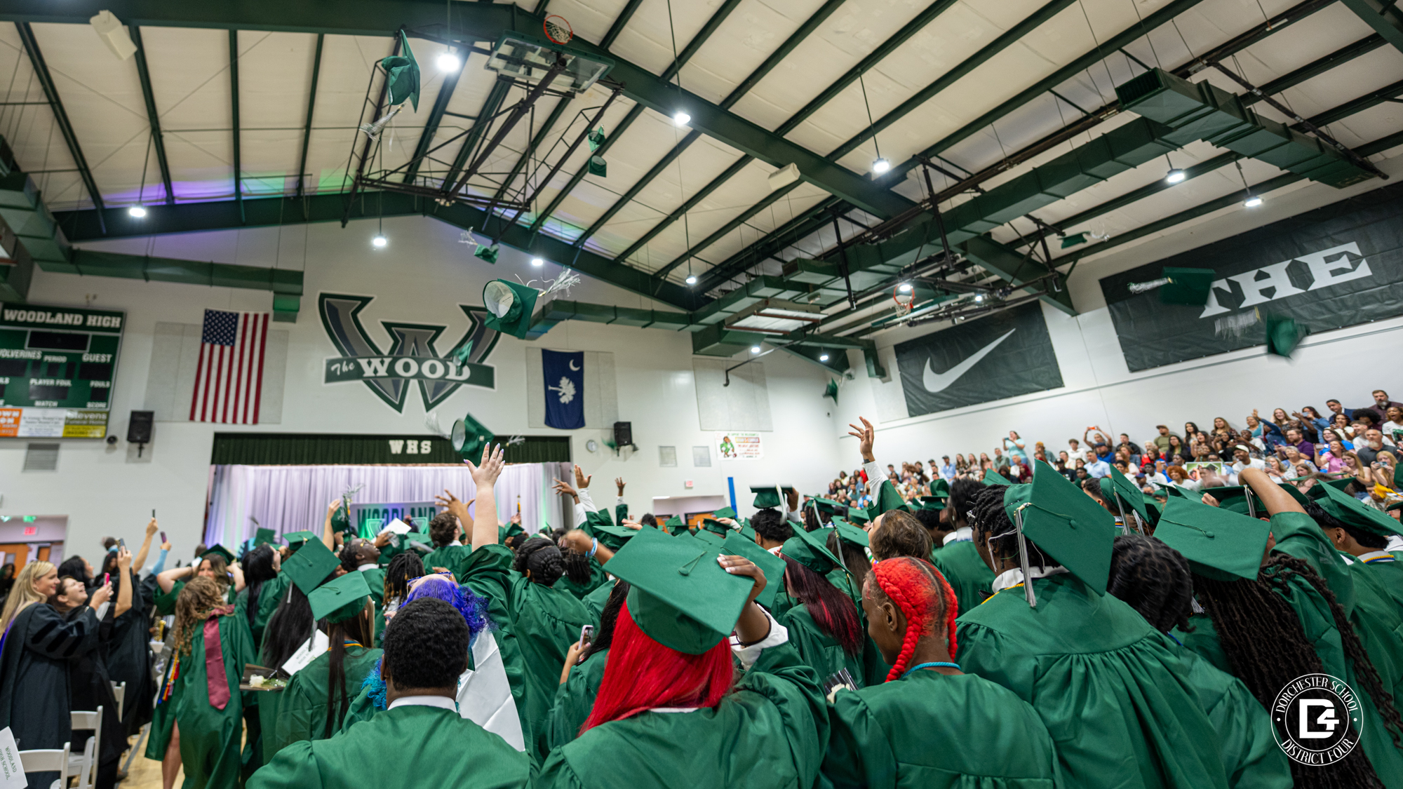 Woodland high school graduation, students are in the gymnasium dressed in green graduate robes and throwing their caps into the air after being confirmed. 
