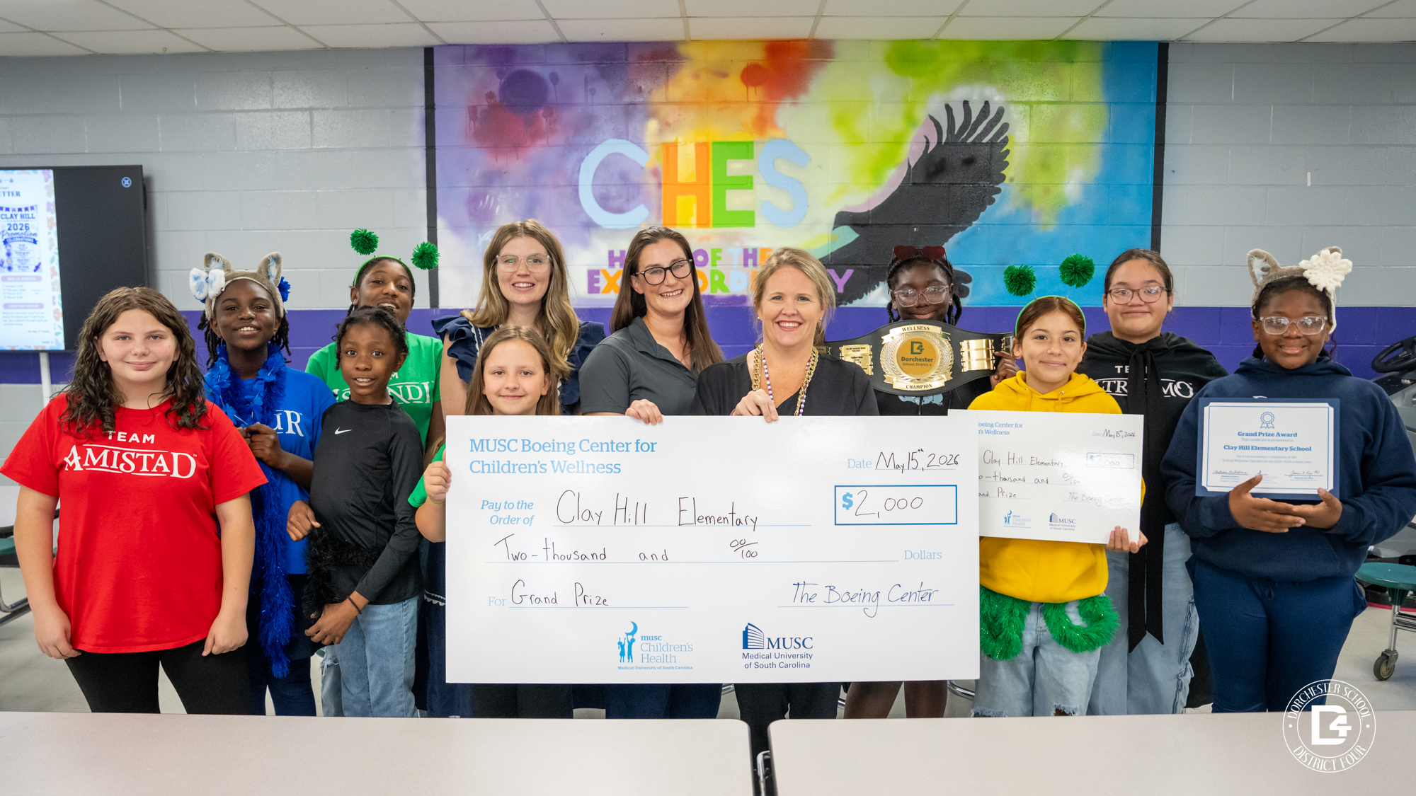 Clay Hill Elementary students, MUSC representatives, and school staff gather together holding the $2,000 MUSC Boeing Center for Children’s Wellness award check and certificate while Nurse Weathers displays the district wellness championship belt.