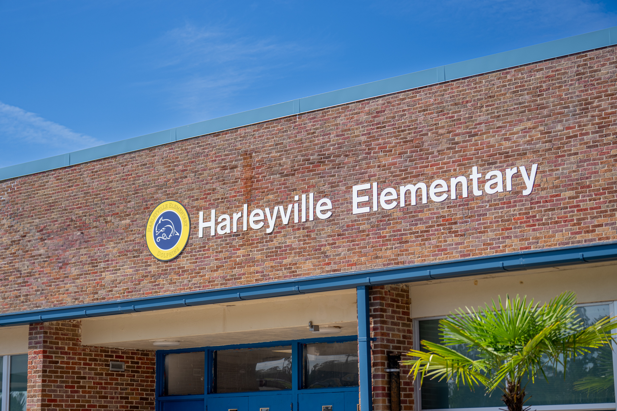 Front entrance of Harleyville Elementary School, featuring the school’s name in white letters and the dolphin mascot logo on a brick building under a clear blue sky.          Ask ChatGPT