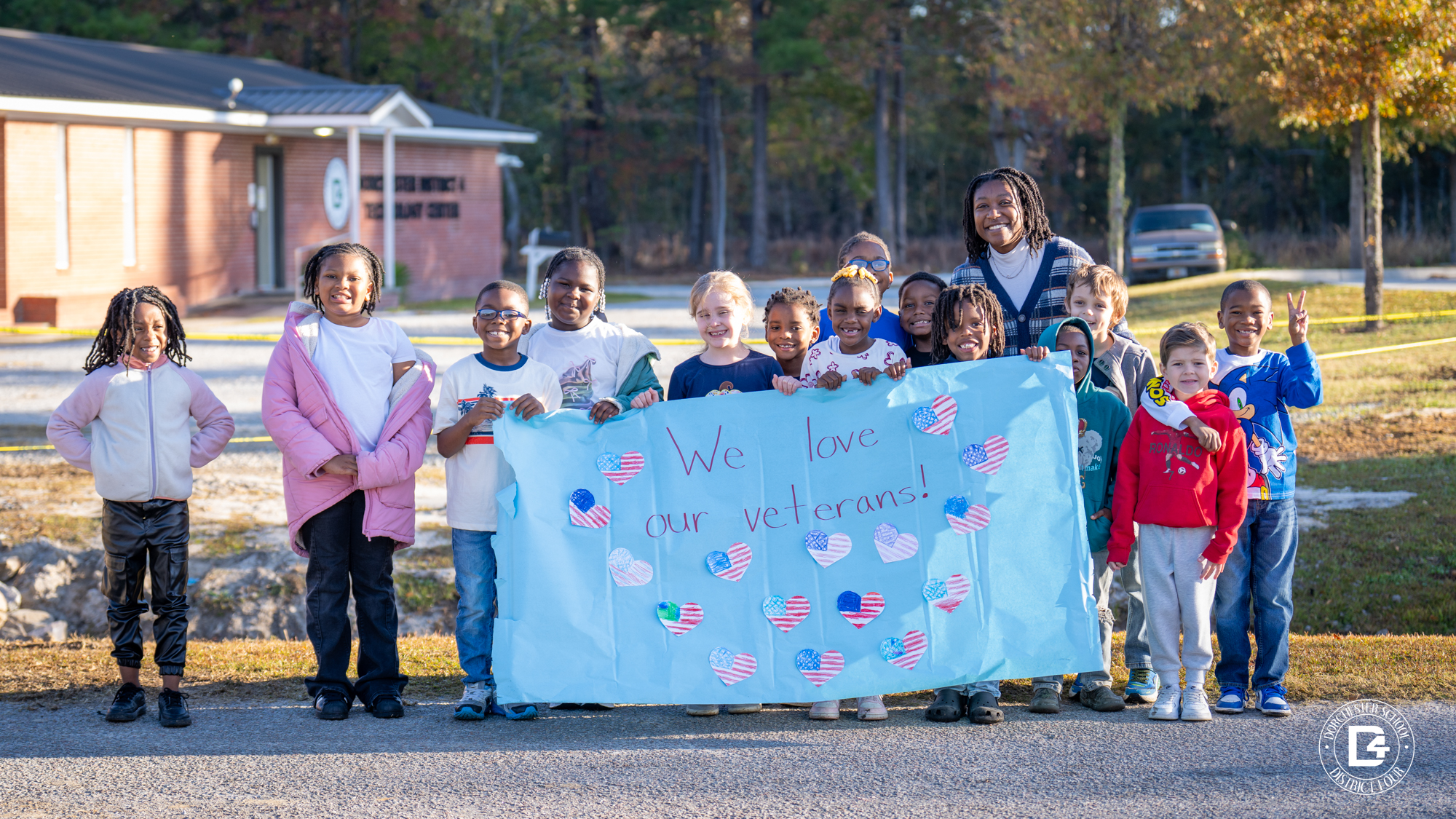 a group of students standing outside of WMES holding a sign thanking veterans at the WMES veterans parade. 