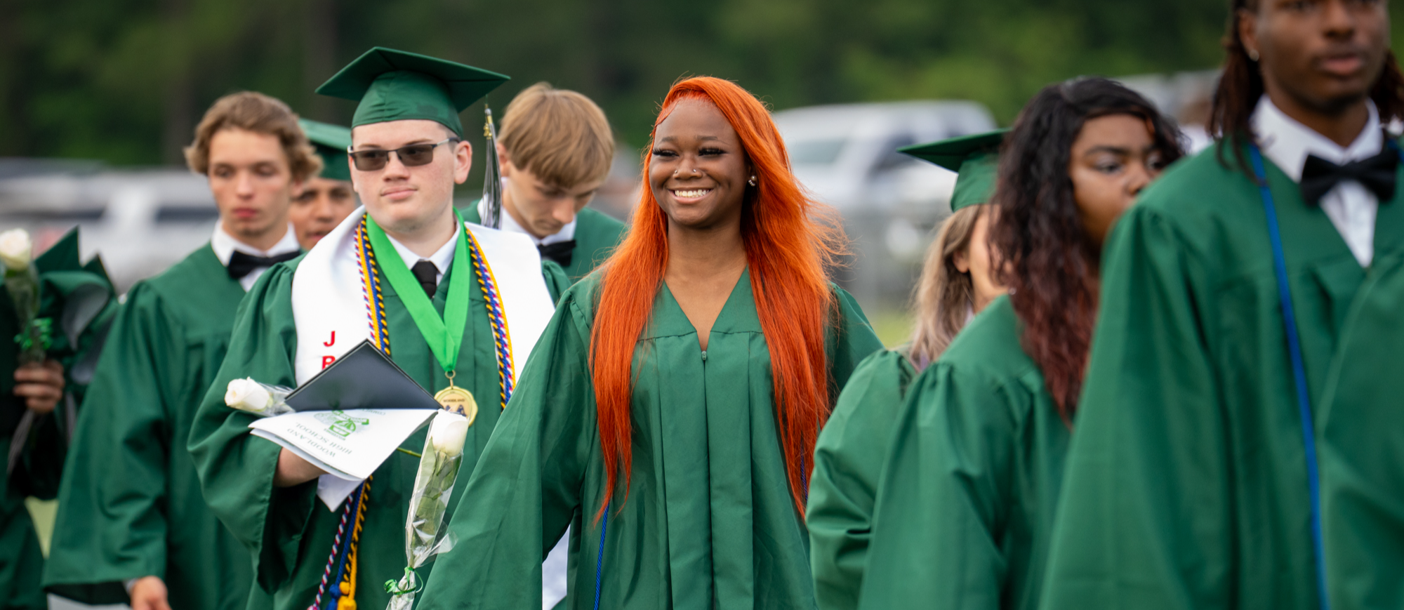 Female student with red hair, smiling as the graduates exit the field. 