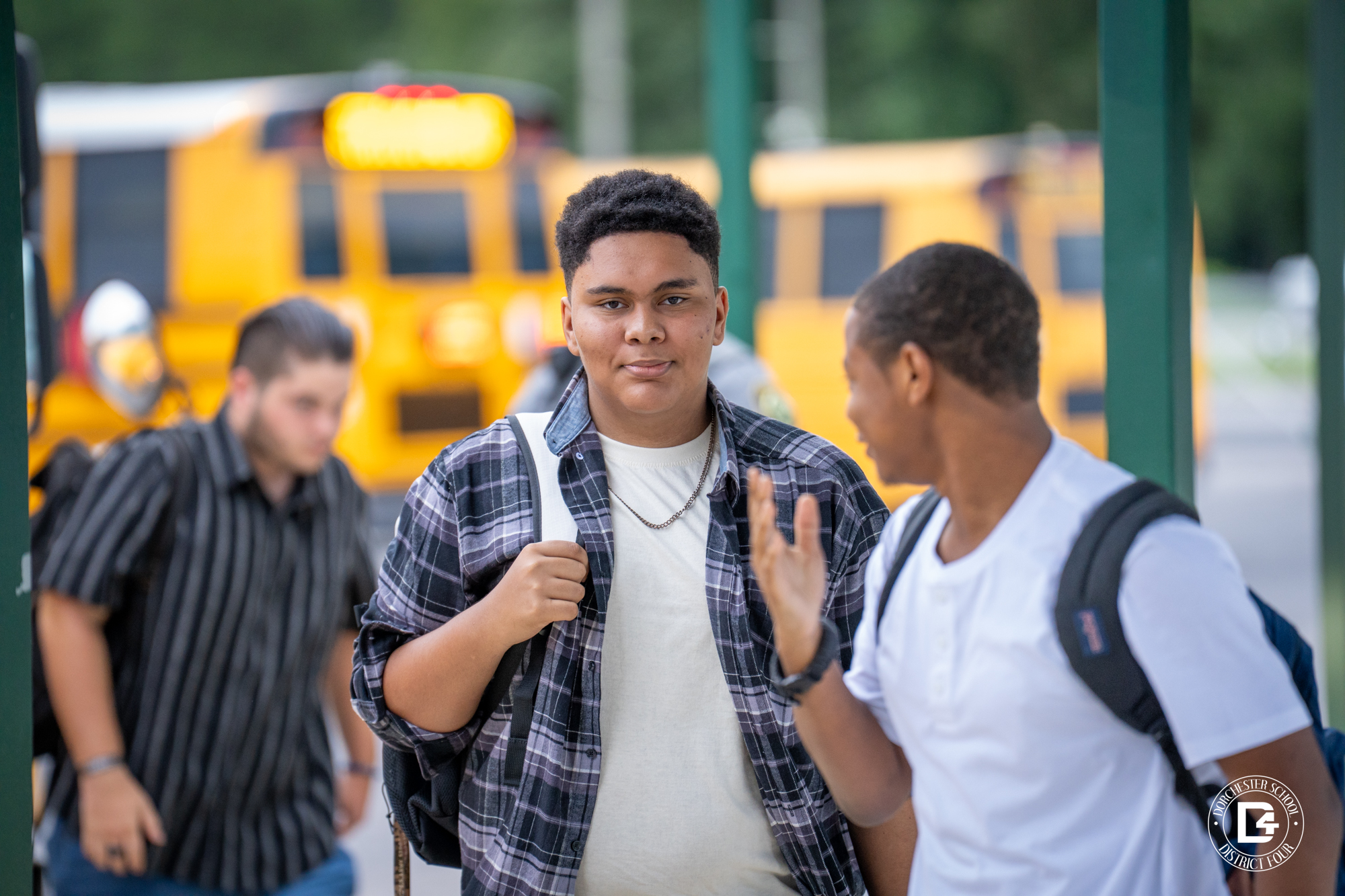 Woodland High School students arrive from the bus area, with one student in a plaid shirt walking alongside a friend.