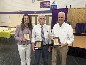 Three individuals proudly display their awards in a gymnasium, celebrating their achievements in a vibrant atmosphere.