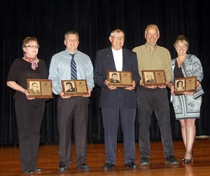 A diverse group of individuals proudly displaying plaques on stage, celebrating their achievements in a formal setting.