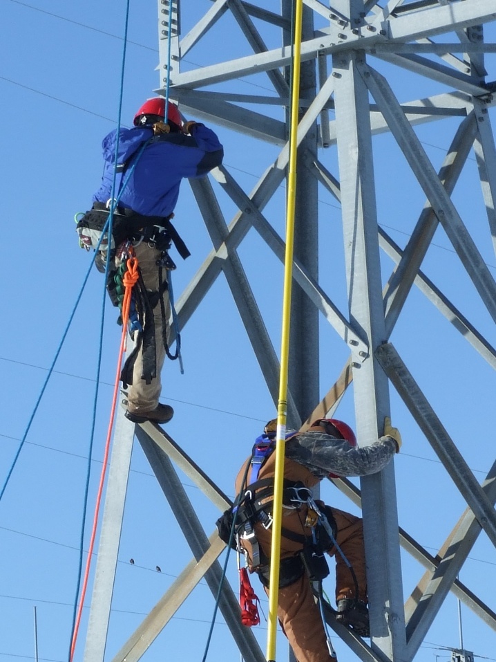 Two utility workers maintaining a power line tower.