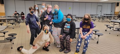 A group of people wearing masks and sitting at tables in a cafeteria.