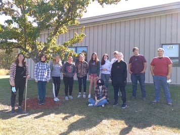 A diverse group of people standing in front of a tall tree, smiling and posing for a photo.