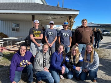 Group of people smiling in front of a rustic barn, capturing a happy moment together.