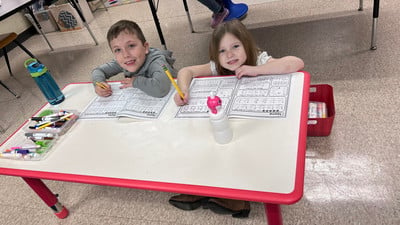 Two children sitting at a table, focused on their schoolwork.