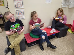 Three children sitting on a bench, engrossed in reading books.