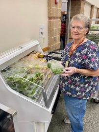 A woman stands beside a refrigerator filled with various food items