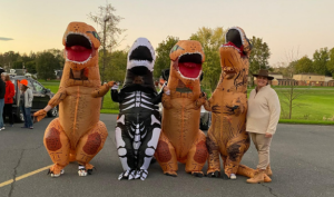 Three people wearing colorful dinosaur costumes stand side by side