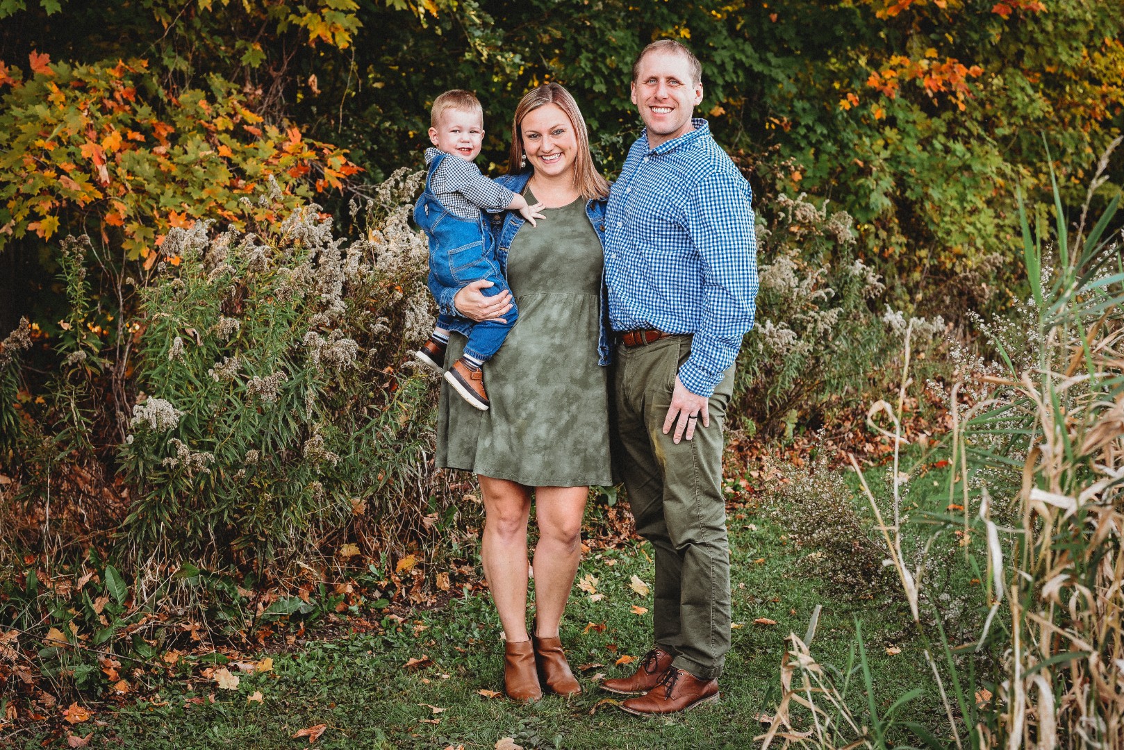 A family smiling for a photo in front of a field of tall grass.