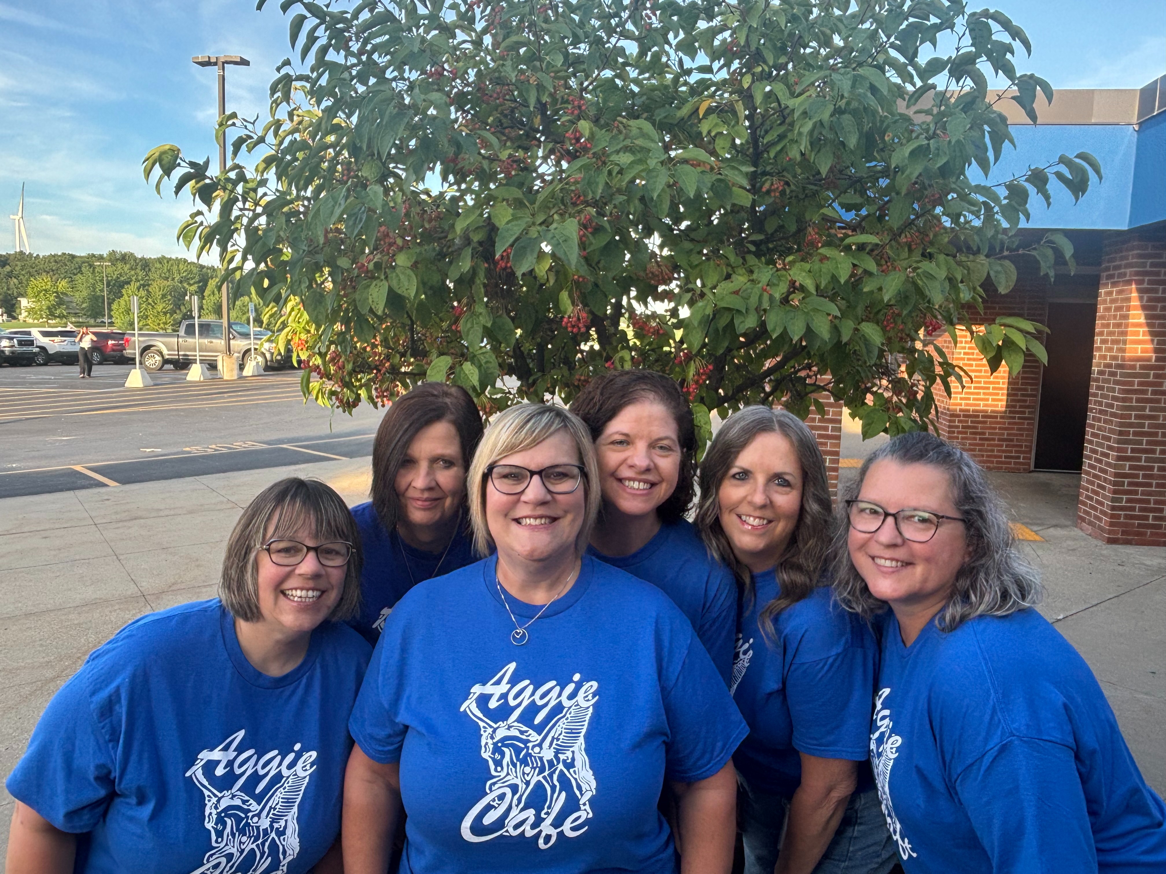 Several women in blue shirts posing in front of a tree.
