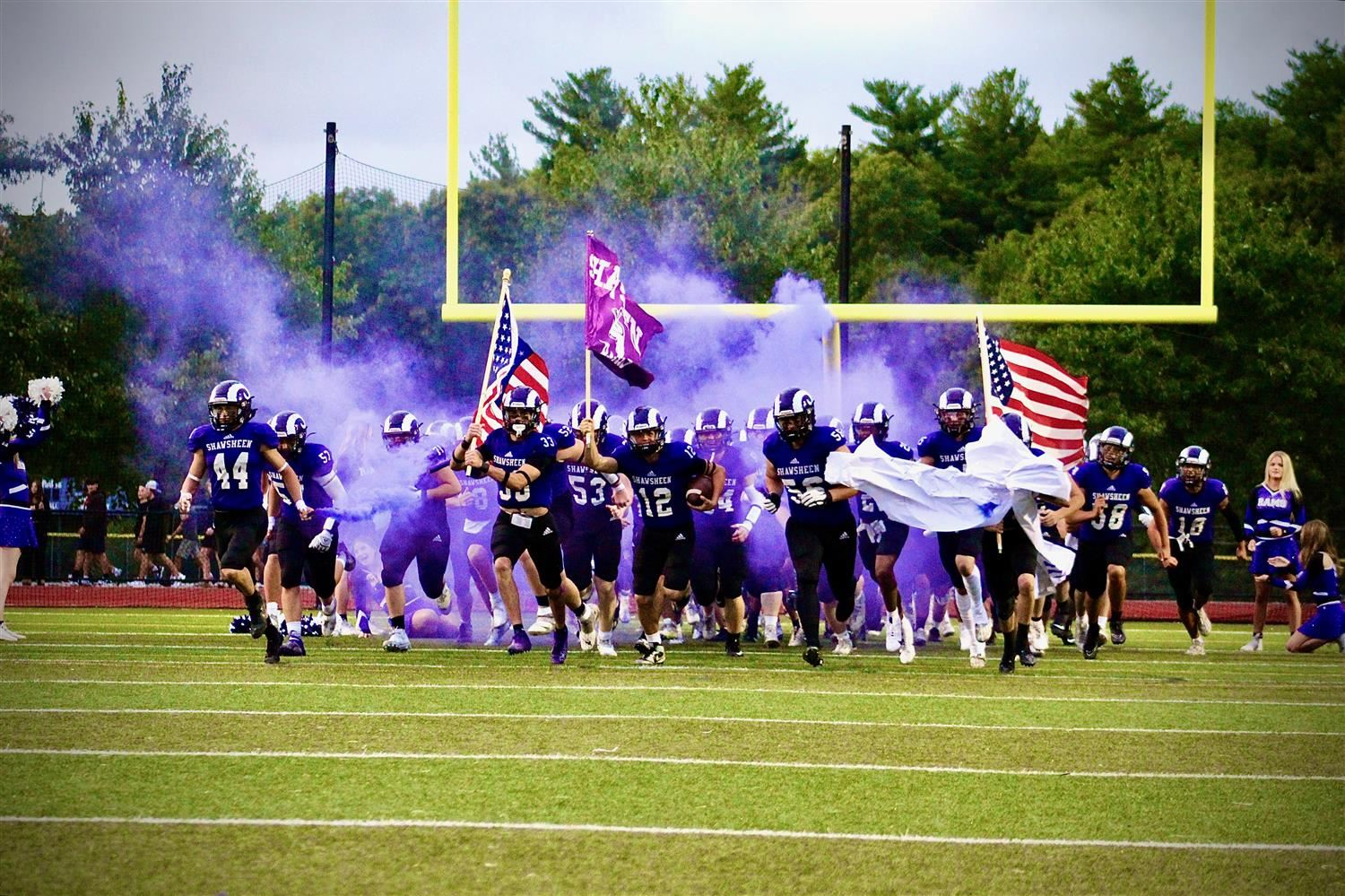 A football team celebrating with purple smoke and waving flags, showcasing team spirit and excitement during a match.