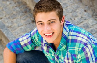 A young man in a plaid shirt sitting on steps outdoors.