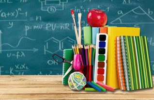 A table filled with various school supplies, with a chalkboard visible in the background, creating an educational atmosphere.