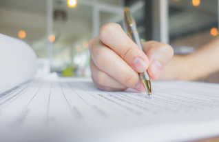 A close-up of a hand writing on a sheet of paper with a pen, capturing the act of note-taking or drafting a letter.