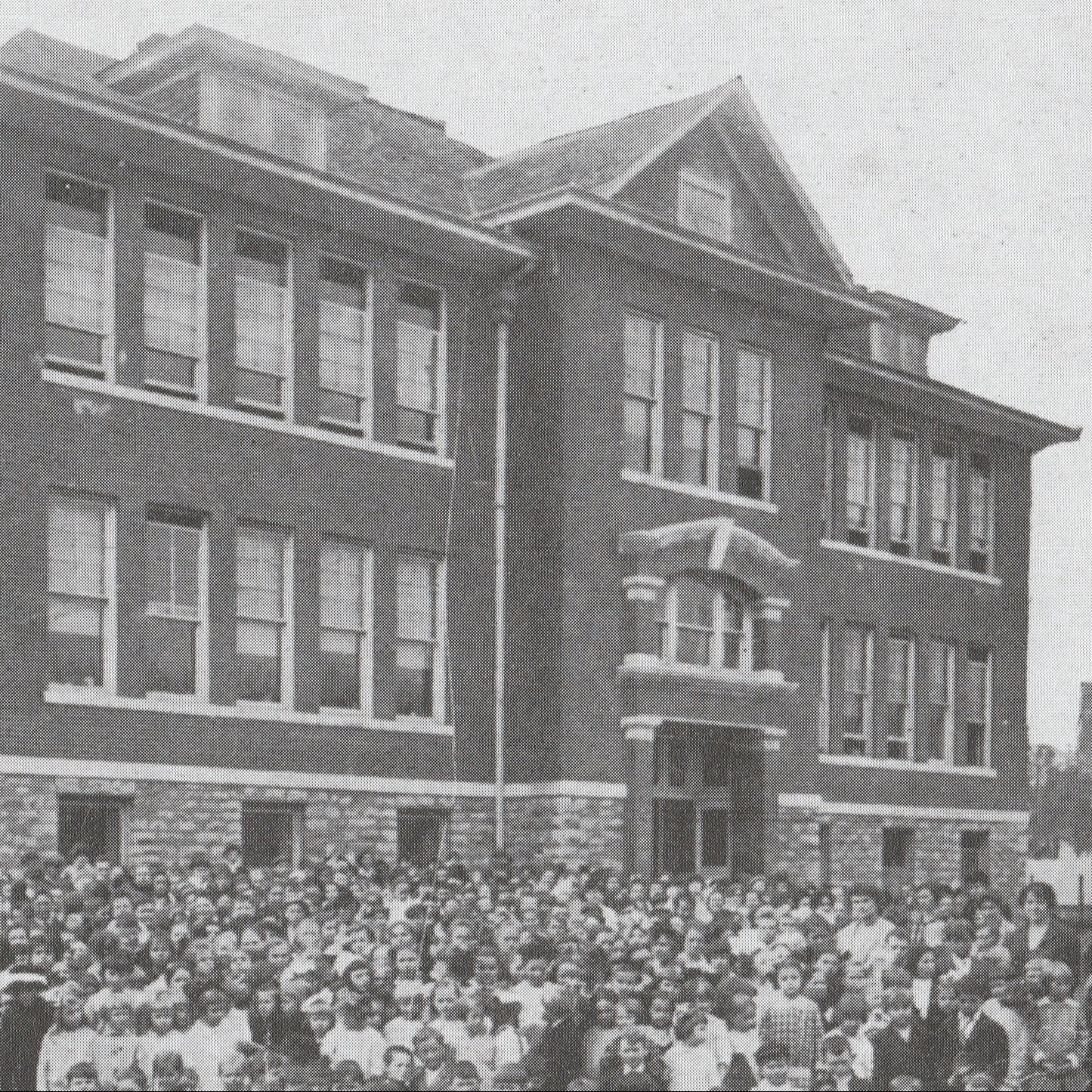 Black-and-white photograph of a school building with a crowd of people gathered outside, published by the Siloam Springs Museum.