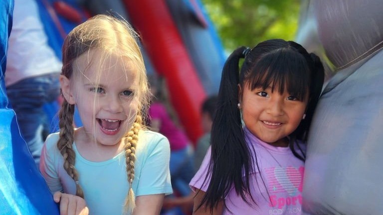 Two young girls stand at an inflatable slide. One wears a blue shirt and the other a purple shirt.